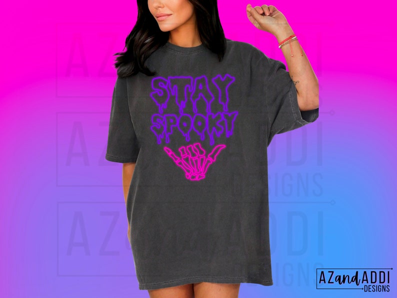 May include: A black t-shirt with a purple and pink graphic that says "Stay Spooky" with a skeleton hand giving a shaka sign.