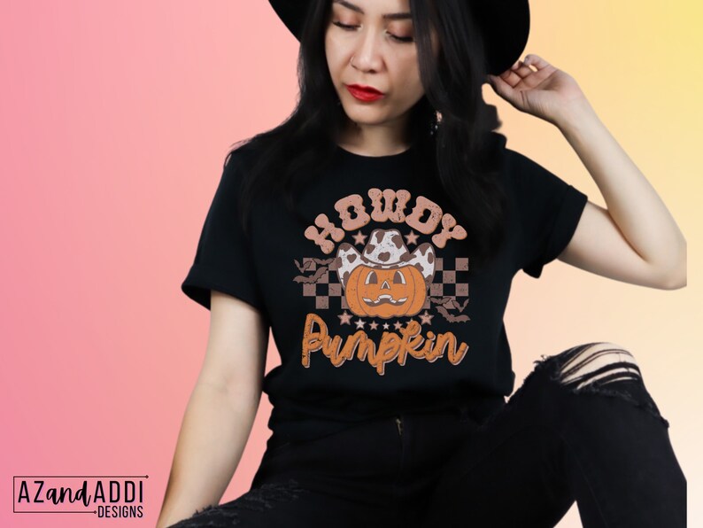May include: Black t-shirt with a Halloween-themed graphic. The design features a pumpkin wearing a cowboy hat, the text "Howdy Pumpkin", and a checkered pattern. The shirt is a short-sleeved crew neck.