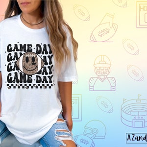 May include: White t-shirt with the text "GAME DAY" in a retro font, featuring a football with a smiley face. The design includes a black and white checkered pattern and stars. The background has football-themed illustrations.