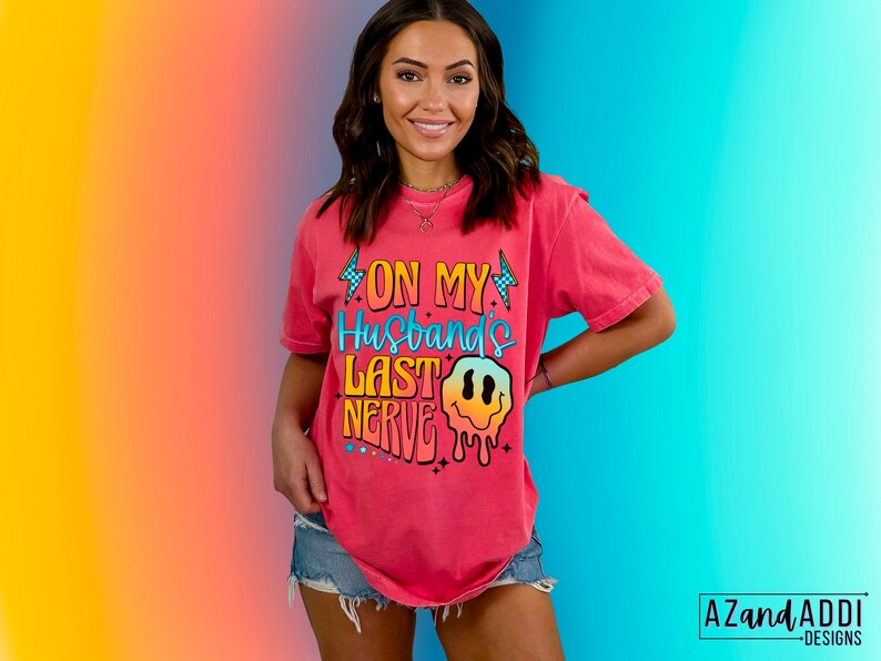 May include: A pink t-shirt with a graphic design that says "On My Husband's Last Nerve" with a dripping smiley face.