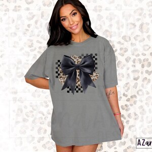 May include: A gray oversized t-shirt with a black bow on a checkered and leopard print background.
