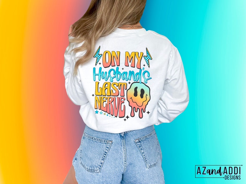 May include: White long-sleeve sweatshirt with a rainbow graphic that says "On My Husband's Last Nerve" with a dripping smiley face.