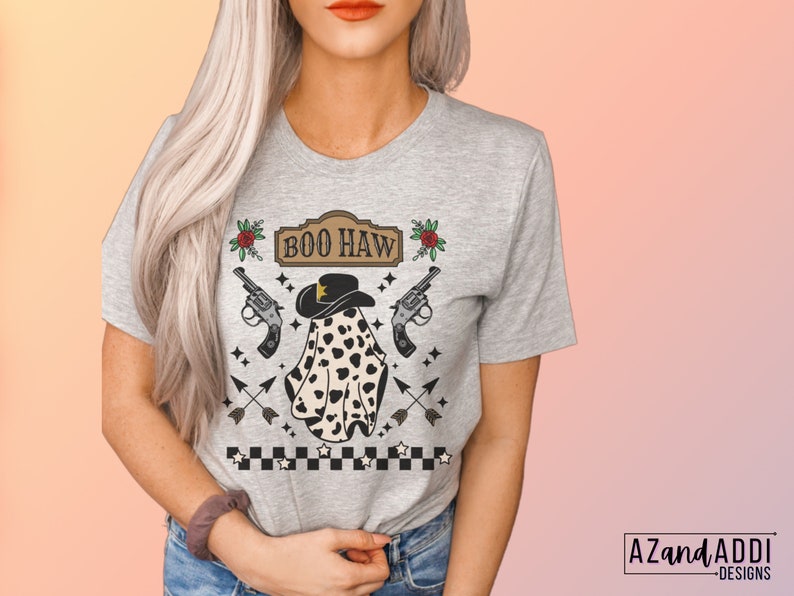 Puede incluir: Una camiseta gris con un fantasma que lleva un sombrero de vaquero y un patr&oacute;n de lunares blanco y negro. El texto "BOO HAW" est&aacute; por encima del fantasma. Tambi&eacute;n hay rosas rojas, pistolas y flechas en la camiseta.
