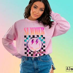May include: Pink sweatshirt with a graphic print of a smiley face with lightning bolts and the text "Summer Babe" in a checkered pattern.