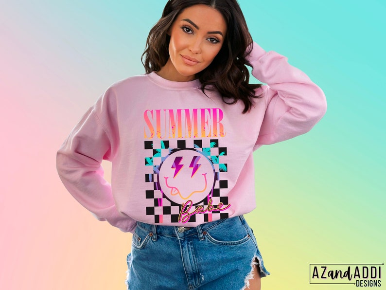 May include: Pink sweatshirt with a graphic print of a smiley face with lightning bolts and the text "Summer Babe" in a checkered pattern.