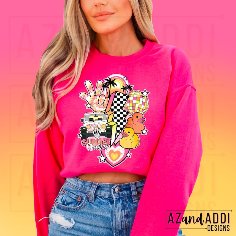 May include: Pink sweatshirt with a graphic design featuring a cartoon jeep, palm trees, a peace sign, a disco ball, lightning bolts, and rubber duckies. The text "Sunset Chapter" is included in the design.