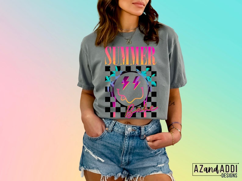 May include: A gray cropped t-shirt with a colorful graphic design that says "Summer Babe" with a smiley face and palm trees. The graphic is on a checkered background.