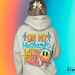 May include: A white hoodie with a colorful graphic on the back that says "On My Husband's Last Nerve" with a dripping smiley face.