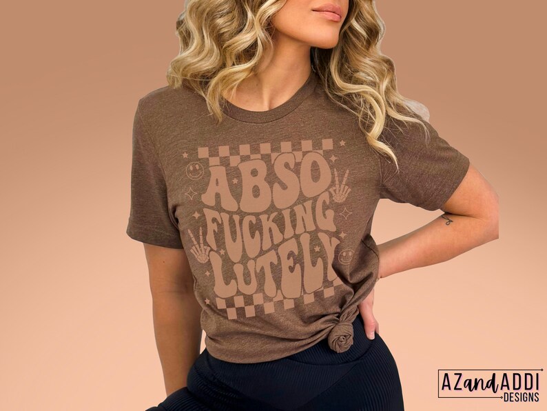 May include: A brown t-shirt with the text "Abso Fucking Lutely" in a retro font with a checkered background.