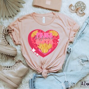 May include: A pink t-shirt with a graphic of a heart with fries and the text "Fries before guys" inside the heart.