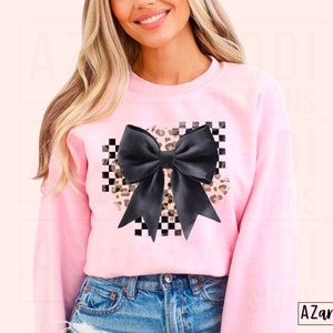 May include: Pink sweatshirt with a black and white checkered design and a large black bow with a leopard print overlay.