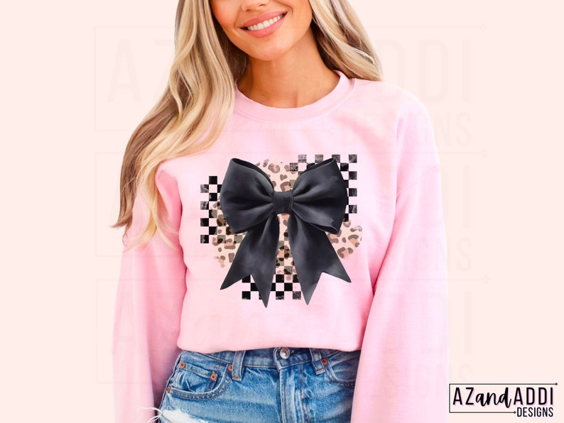 May include: Pink sweatshirt with a black and white checkered design and a large black bow with a leopard print overlay.