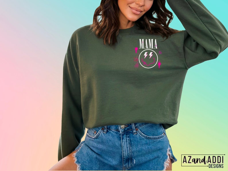 Pu&ograve; includere: Felpa verde con una grafica bianca di un viso sorridente con fulmini e la parola "MAMA" sopra.