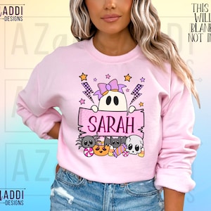 K&ouml;nnte beinhalten: Ein hellrosa Sweatshirt mit einem Halloween-Motiv. Das Design zeigt einen Geist, der ein Schild mit dem Namen "SARAH" h&auml;lt, umgeben von Sternen, Blitzen und Halloween-S&uuml;&szlig;igkeiten. Der Text "THIS DESIGN WILL COME BLANK. NAME NOT INCLUDED" ist ebenfalls sichtbar.