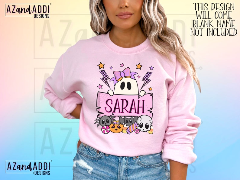 K&ouml;nnte beinhalten: Ein hellrosa Sweatshirt mit einem Halloween-Motiv. Das Design zeigt einen Geist, der ein Schild mit dem Namen "SARAH" h&auml;lt, umgeben von Sternen, Blitzen und Halloween-S&uuml;&szlig;igkeiten. Der Text "THIS DESIGN WILL COME BLANK. NAME NOT INCLUDED" ist ebenfalls sichtbar.