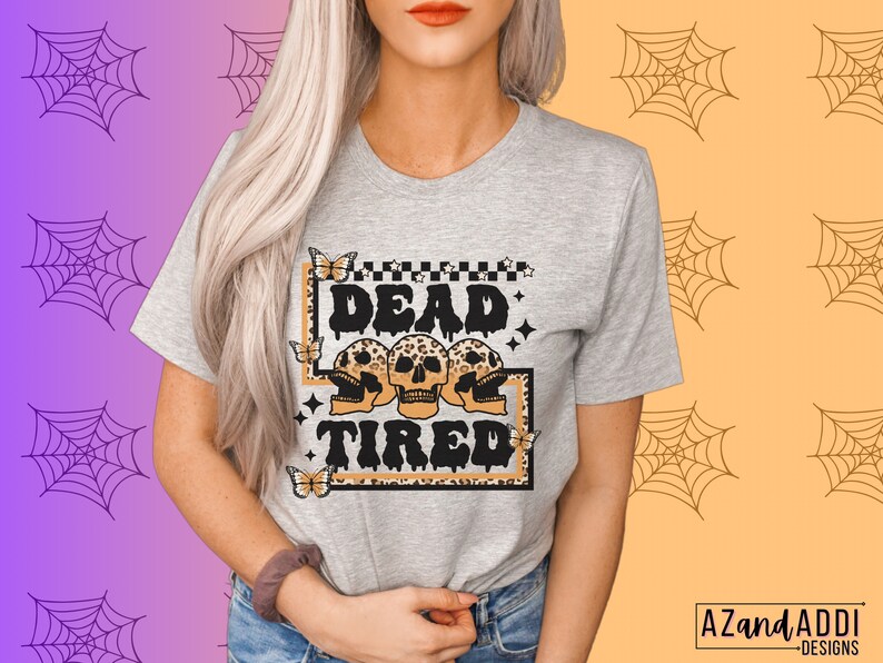 Op de afbeelding: Een grijs T-shirt met een grafische print van drie schedels met luipaardprint en de tekst "Dead Tired".