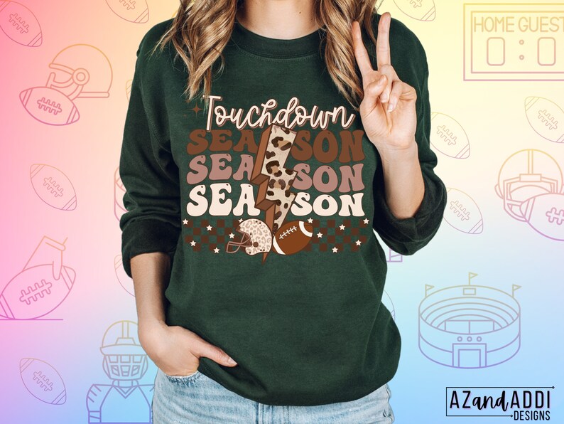 May include: Green sweatshirt with the text "Touchdown Season" in brown, pink, and white lettering. The text is layered with a brown and black leopard print and a lightning bolt graphic.