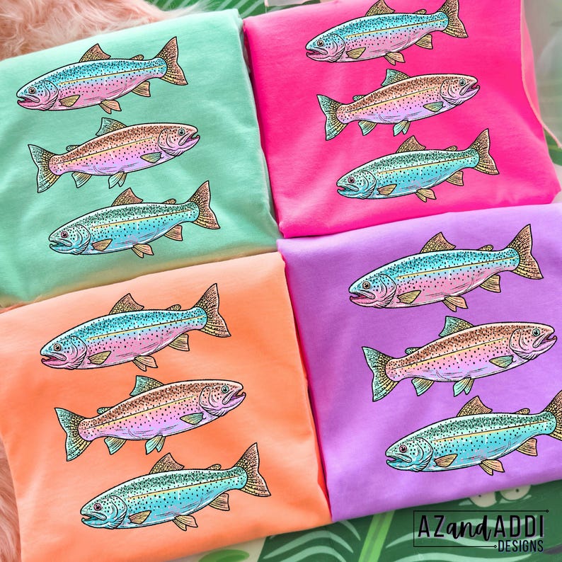 Puede incluir: Varias camisetas de colores brillantes en tonos rosa, verde, naranja y morado, cada una con una ilustraci&oacute;n detallada de una trucha. Los peces est&aacute;n representados con escamas azules, rosas y marrones. La camiseta inferior derecha tiene el texto "AZandADDI DESIGNS".