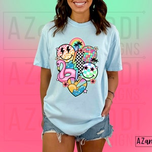 May include: A light blue t-shirt with a colorful graphic print of a flamingo, smiley faces, a disco ball, and other summer-themed elements.
