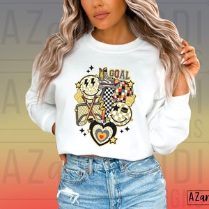 May include: White sweatshirt with a graphic design of a hockey stick, a net, a heart, and a smiley face with the word "GOAL" printed on it.