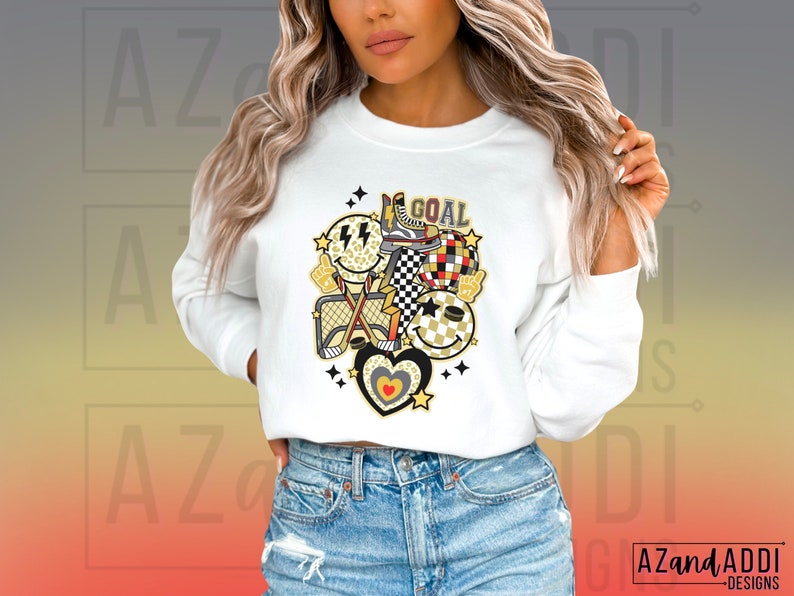 May include: White sweatshirt with a graphic design of a hockey stick, a net, a heart, and a smiley face with the word "GOAL" printed on it.
