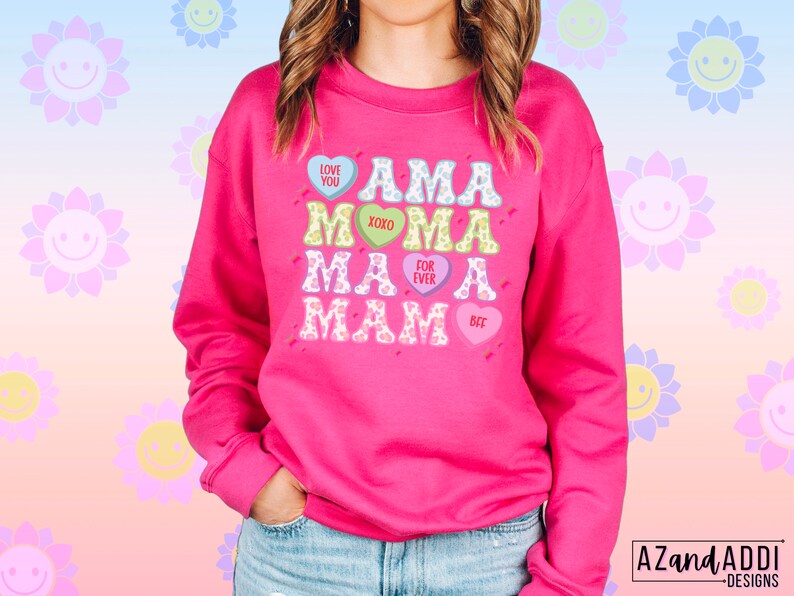 May include: Pink sweatshirt with a graphic design of the word "AMA" repeated four times in different colors and fonts. Each "AMA" is surrounded by a heart with a different message on each heart: "LOVE YOU", "XOXO", "FOR EVER", and "BFF".