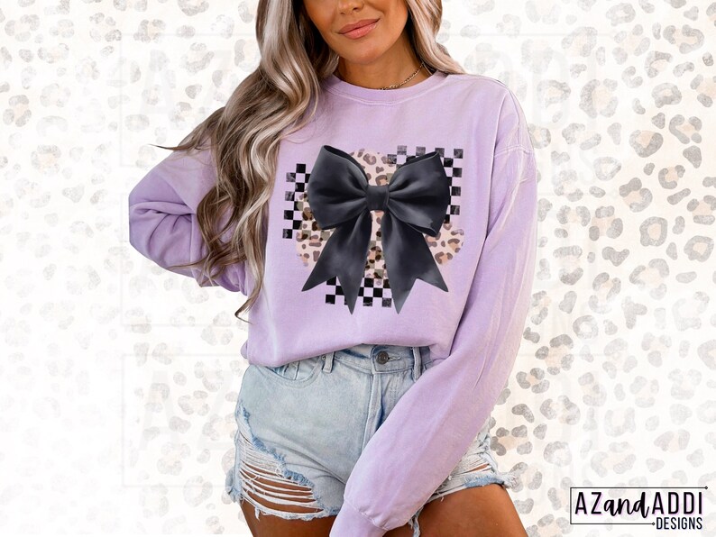 May include: A lavender sweatshirt with a black bow on a checkered and leopard print background.