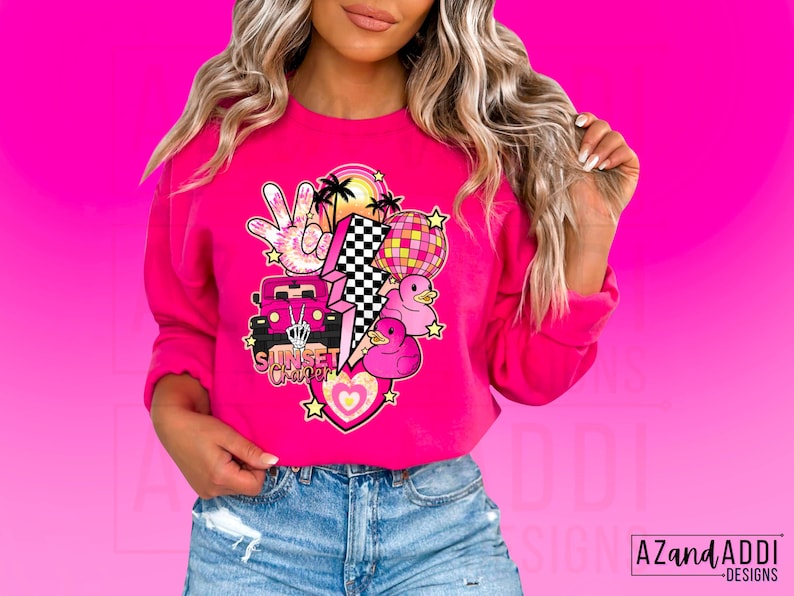 May include: Pink sweatshirt with a graphic design featuring a pink car, a lightning bolt, a peace sign, a disco ball, and rubber ducks. The text "Sunset Cruiser" is included in the design.