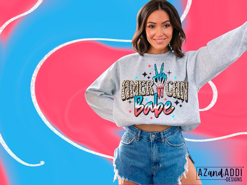 May include: A grey sweatshirt with a red, white and blue peace sign with the text "American Babe" in a glittery font. The peace sign is surrounded by a leopard print pattern.