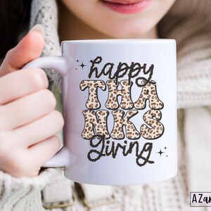 May include: White ceramic mug with a black and brown leopard print design that says "happy THANKS giving" in black text.
