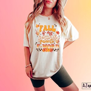 Pu&ograve; includere: T-shirt color crema con la scritta "Fall is my second favorite F-WORD" in arancione e giallo. Il design include foglie autunnali e un motivo a scacchi. La maglietta &egrave; di vestibilit&agrave; ampia.