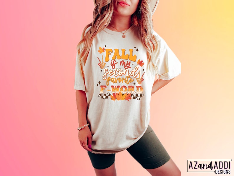 Pu&ograve; includere: T-shirt color crema con la scritta "Fall is my second favorite F-WORD" in arancione e giallo. Il design include foglie autunnali e un motivo a scacchi. La maglietta &egrave; di vestibilit&agrave; ampia.