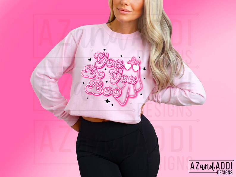 K&ouml;nnte beinhalten: Hellrosa Langarmshirt mit dem Schriftzug "You Do You Boo" in einem Retro-Schriftstil. Das Design beinhaltet einen Geist, Herzen und Sterne. Das Shirt hat einen verk&uuml;rzten Stil.