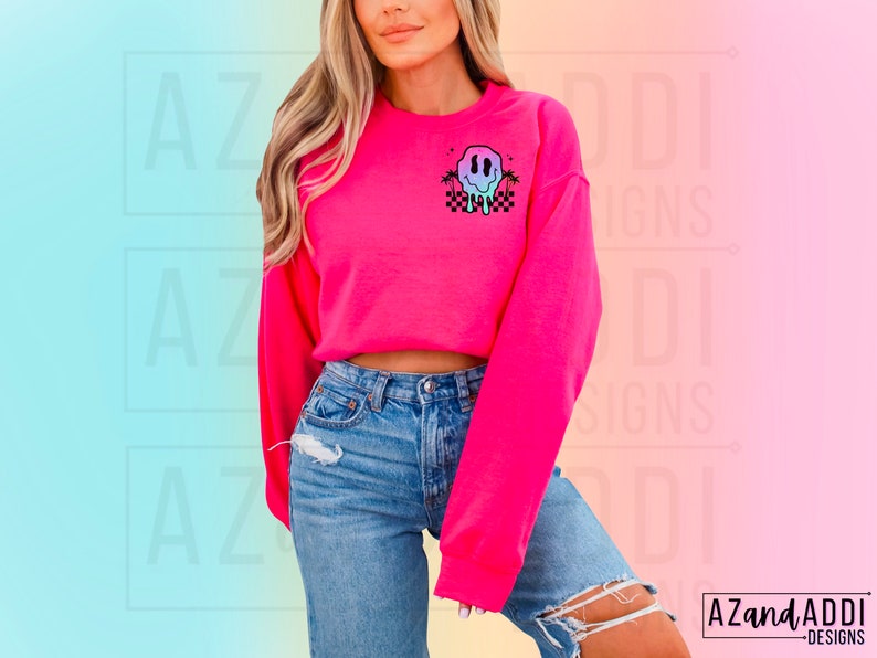 May include: A pink cropped sweatshirt featuring a graphic of a melting smiley face with palm trees and a checkered pattern. The sweatshirt is being worn by a person with long blonde hair.