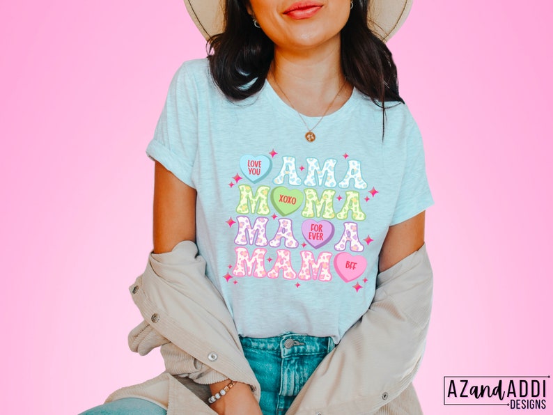 May include: A light blue t-shirt with a graphic design of the word "MAMA" spelled out with candy hearts. The hearts have different colors and sayings like "Love You", "XOXO", "For Ever", and "Bet".