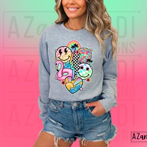 May include: A gray sweatshirt with a colorful graphic print featuring a flamingo, smiley faces, a rainbow, a checkered pattern, and a palm tree. The graphic is centered on the front of the sweatshirt.