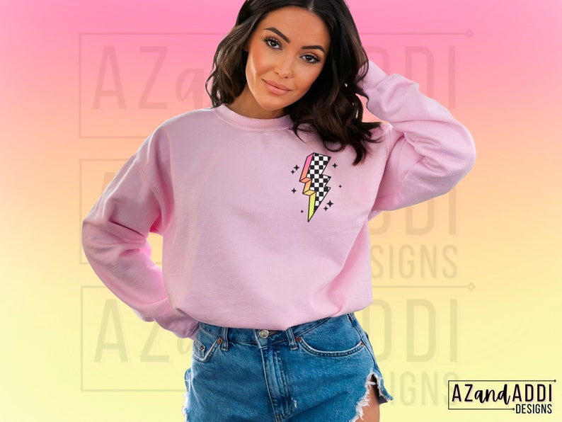 K&ouml;nnte beinhalten: Rosafarbener Pullover mit einem karierten Blitz-Motiv. Das Motiv ist in den Farben Rosa, Gelb und Schwarz gehalten.