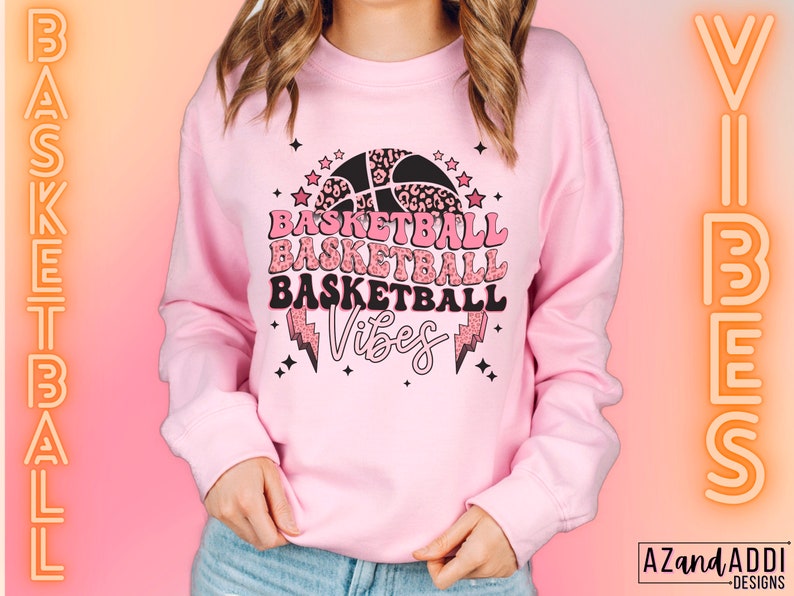 May include: A light pink sweatshirt with a basketball-themed graphic. The graphic includes the word "Basketball" repeated three times, a basketball, stars, and lightning bolts. The word "Vibes" is also included.
