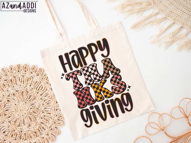 May include: A white canvas tote bag with the text "Happy Thanks Giving" in black and colorful checkered letters. The letters are in a retro style font.