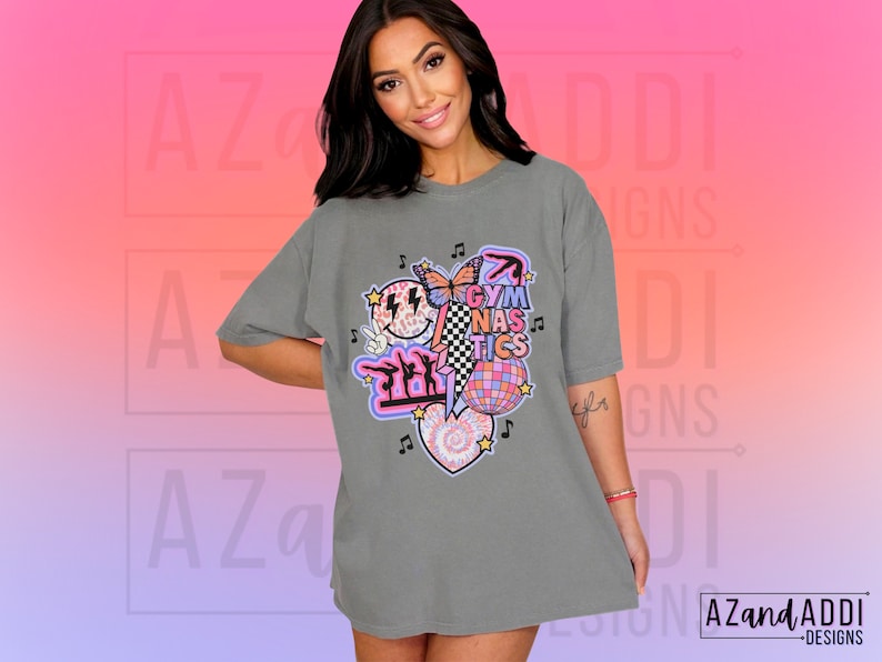 May include: A gray oversized t-shirt with a graphic design featuring a pink heart, a disco ball, a butterfly, a checkered pattern, and the text "Gymnastics".