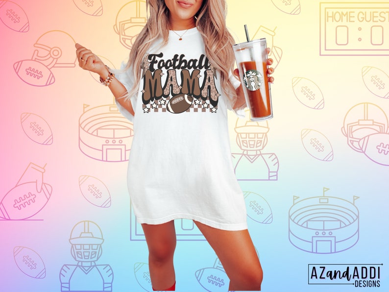 Pode incluir: Camiseta branca com texto marrom que diz "Football Mama" com um gr&aacute;fico de futebol e um padr&atilde;o xadrez. A camiseta &eacute; de tamanho grande e tem um caimento solto.