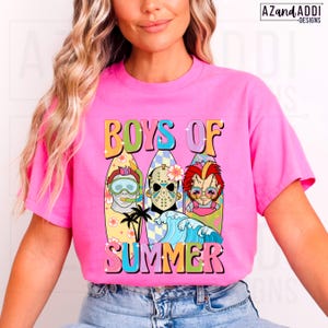 May include: A bright pink t-shirt featuring the words "BOYS OF SUMMER" in a retro font. The graphic includes three surfboards with cartoon characters, a wave, and palm trees. The shirt is a vibrant and eye-catching design.