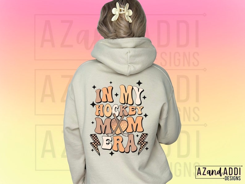 May include: A white hoodie with a graphic on the back that says "In My Hockey Mom Era" in a retro font with a hockey stick and puck design.