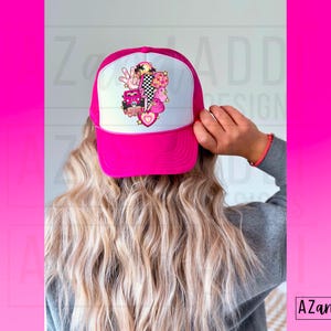 May include: A pink trucker hat with a white mesh back. The hat has a colorful graphic design featuring a heart, a peace sign, a palm tree, and other elements.