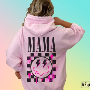 Pu&ograve; includere: Felpa rosa con un designo a scacchi bianco e nero, un'emoticon sorridente rosa con fulmini e la parola "MAMA" in lettere nere.