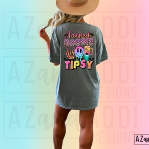 May include: A grey t-shirt with a colourful graphic that says "Tanned Bougie Tipsy" with a smiley face, palm trees, and a drink.