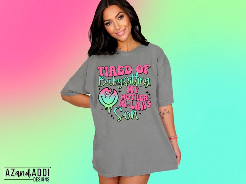 Puede incluir: Camiseta gris con un gr&aacute;fico rosa y azul que dice "Cansado de cuidar al hijo de mi suegra".