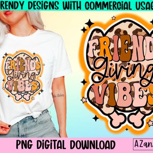 May include: White t-shirt with a colorful graphic that says "FRIENDS Living VIBES". The design features a leopard print background with orange, brown, and pink lettering. The words are outlined in black and surrounded by stars.