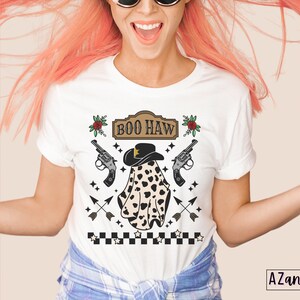Puede incluir: Camiseta blanca con un fantasma blanco y negro que lleva un sombrero de vaquero y el texto "BOO HAW" en una fuente de estilo vintage. El fantasma est&aacute; rodeado de estrellas, flechas y pistolas.