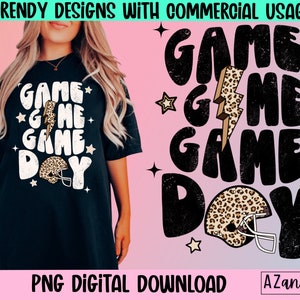 May include: A black t-shirt with a white graphic design that says "GAME GAME DAY" with a lightning bolt and a football helmet with a leopard print design.